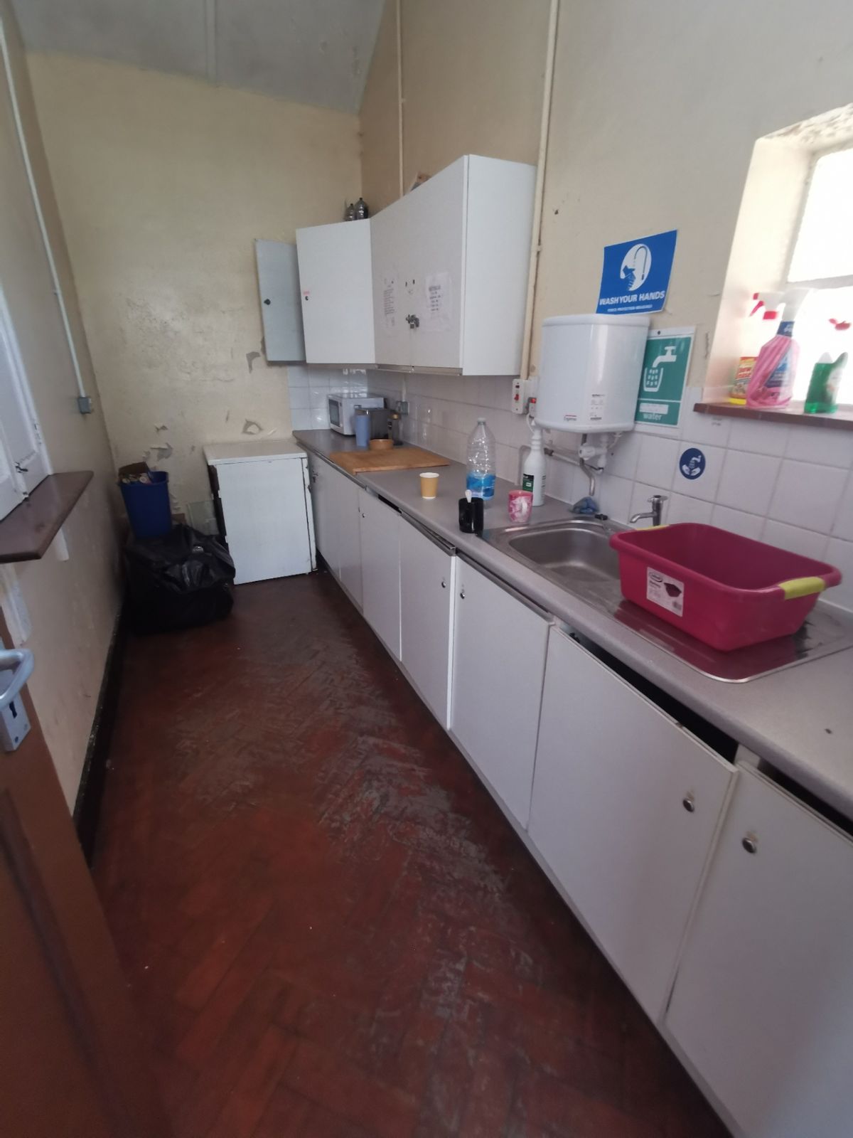 Kitchen with white cupboards, sink, water boiler and hand-wash notices