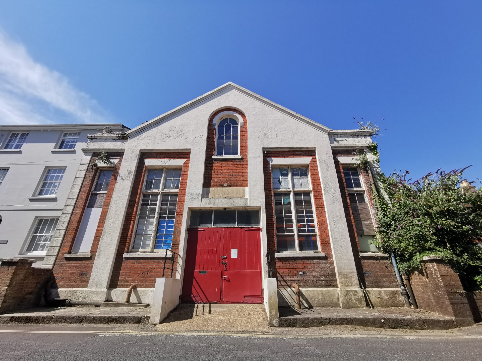 The Drill Hall's Bath Road frontage: white-painted gable, arched window and red entrance doors beneath a blue sky