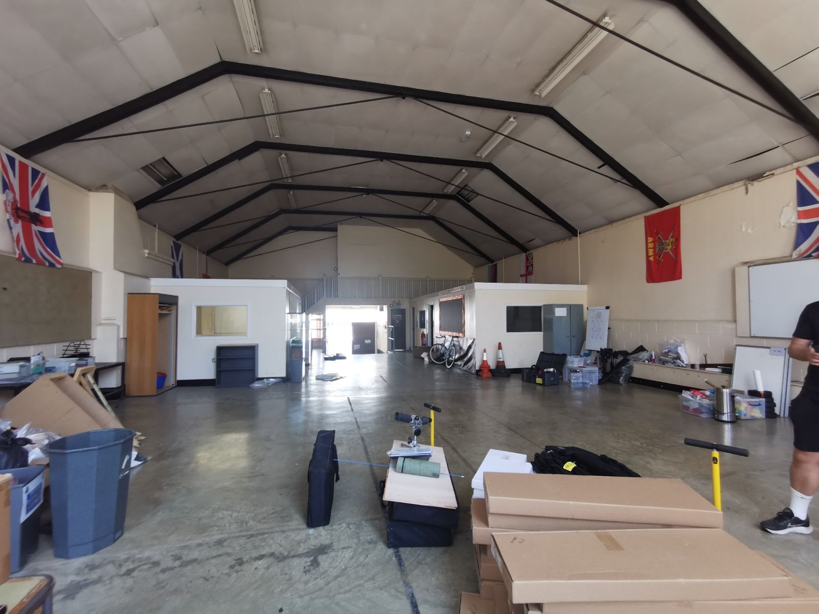 Wide view of the main drill hall interior with steel roof trusses, high windows, regimental flags and the entrance at the far end